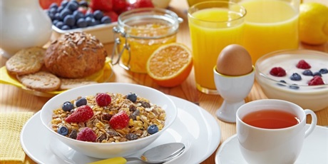 Powiększ grafikę: Stół zastawiony śniadaniowymi artykułami spożywczymi: płatki, owoce, sok, herbata w białej filiżance.