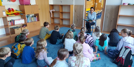 Powiększ grafikę: Uczniowie siedzą na dywanie i słuchają opowiadań o zwierzętach, które czyta im nauczycielka